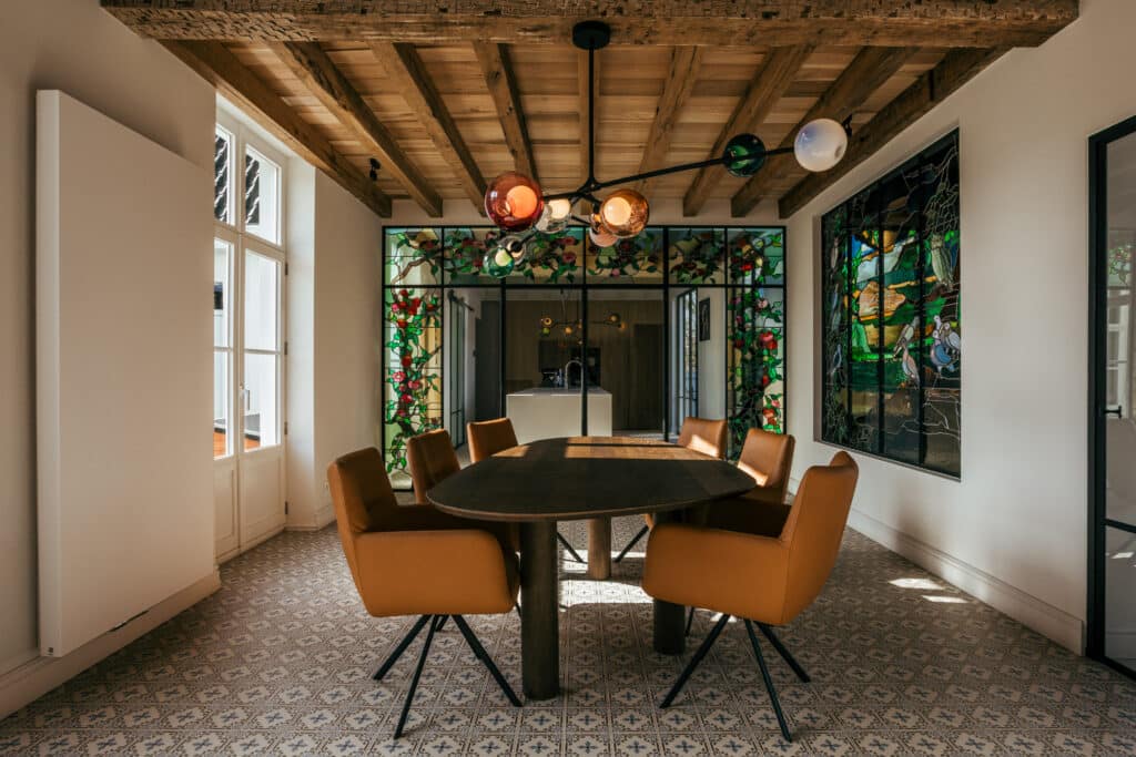 Overzicht van de eetkamer met stalen binnenpuien rond gebrandschilderde glas-in-loodpanelen onder de balken.