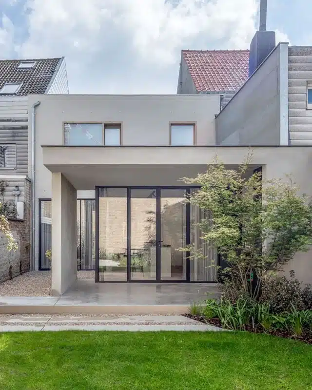 Gerenoveerde achtergevel met een stalen glaspui onder de overdekte terraszone, gezien vanuit de tuin.