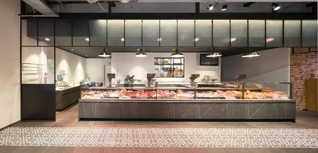 Charcuterie-afdeling van een supermarkt met een zwevende stalen structuur in kathedraalglas boven de toog.