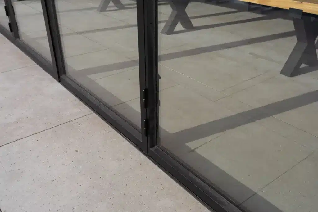Detail van het onderprofiel en de scharnieren van een stalen harmonicadeur op de terrastegels.
