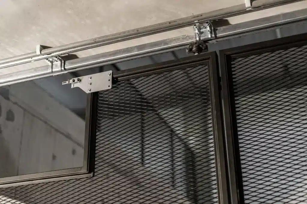 Detail van de ophanging en de rails van de stalen schuifwand in strekmetaal, tegen het betonnen plafond.