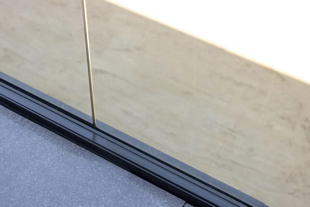Detail van het zwarte bodemprofiel van de glazen balustrade op het terras in natuursteen.