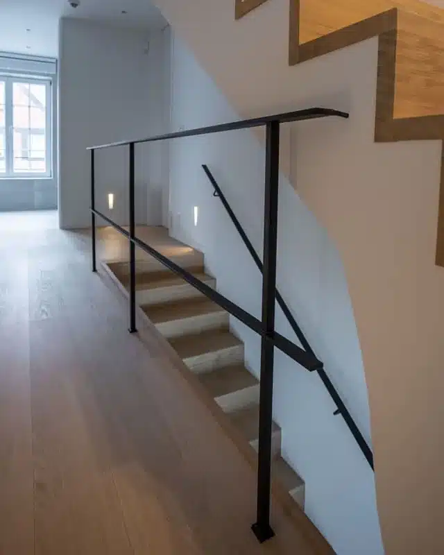 Detail van de slanke volstalen balustrade en de stalen handgreep langs de eiken trap naar beneden.