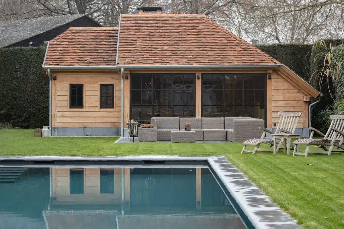 Eiken poolhouse met pannendak aan het zwembad, met een brede stalen raampartij met roedeverdeling.