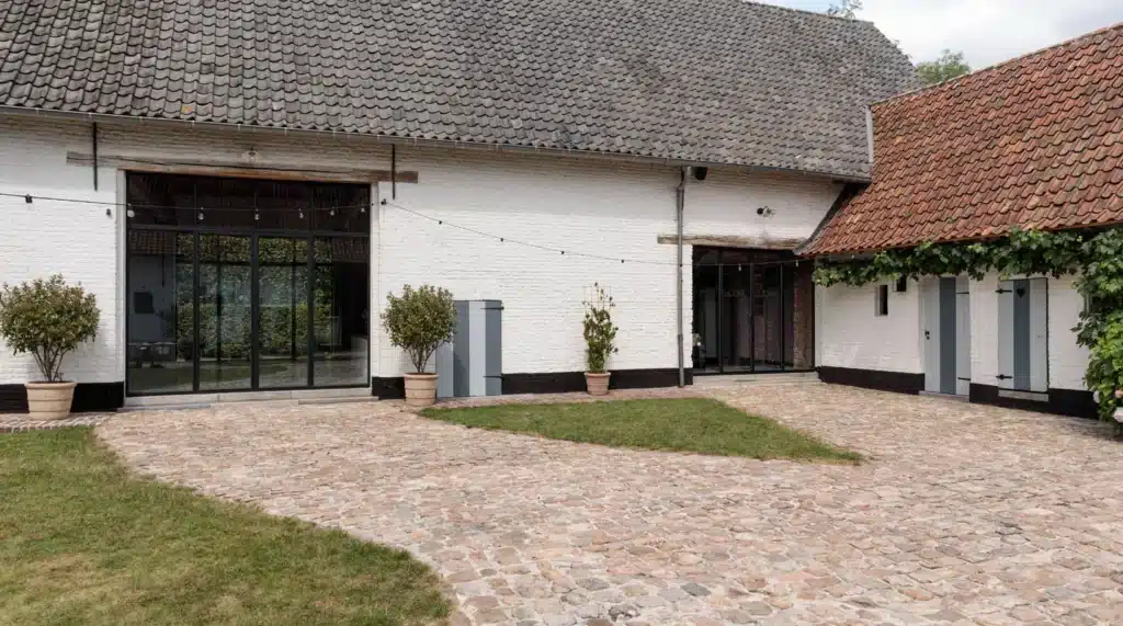 Gerenoveerde hoeve met feestzaal en brede stalen glaspartijen aan de gekasseide binnenkoer.