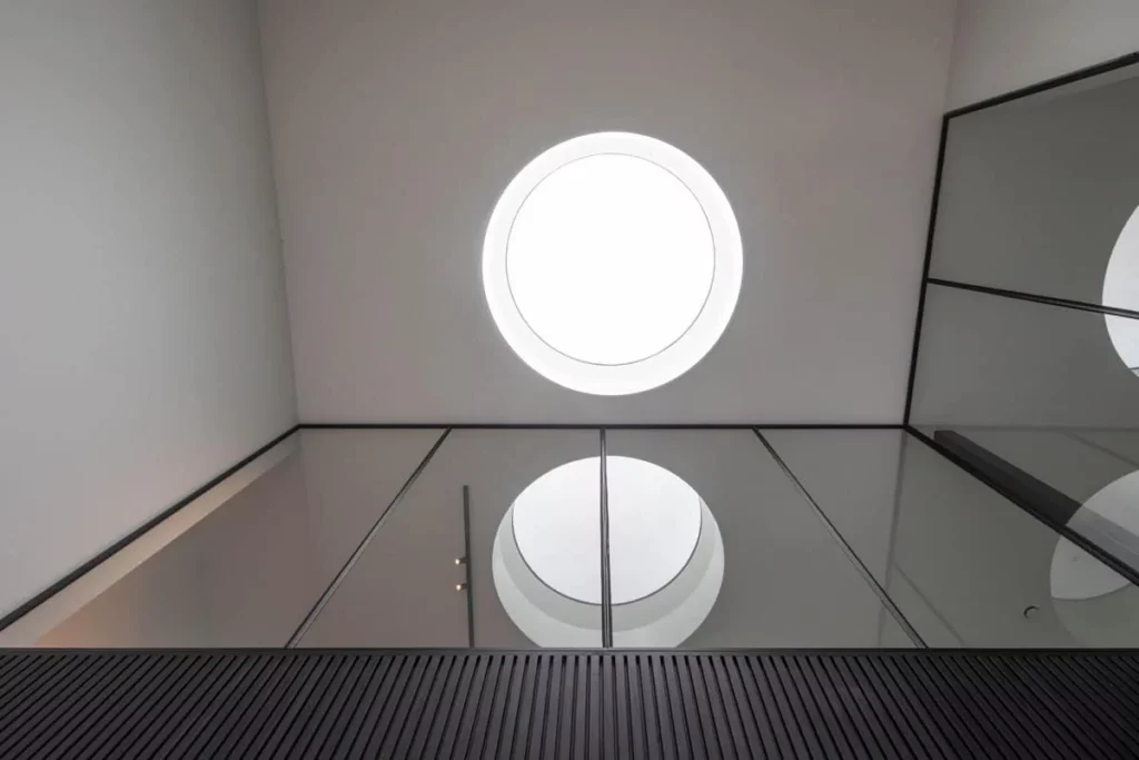 Glazen balustrade rond de vide onder de ronde lichtkoepel, met de stalen glaswand van de verdieping ernaast.