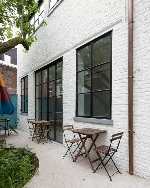 Staand zicht op het witte koetshuis met superslanke stalen ramen en deuren langs het terras.