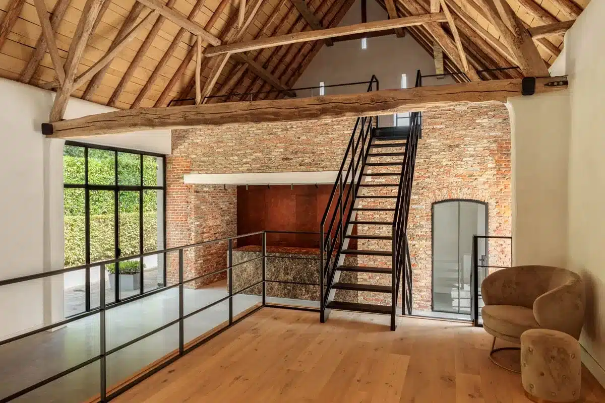 Lounge met houten vloer en stalen borstwering, met de stalen trap en een stalen boogdeur in de bakstenen wand.