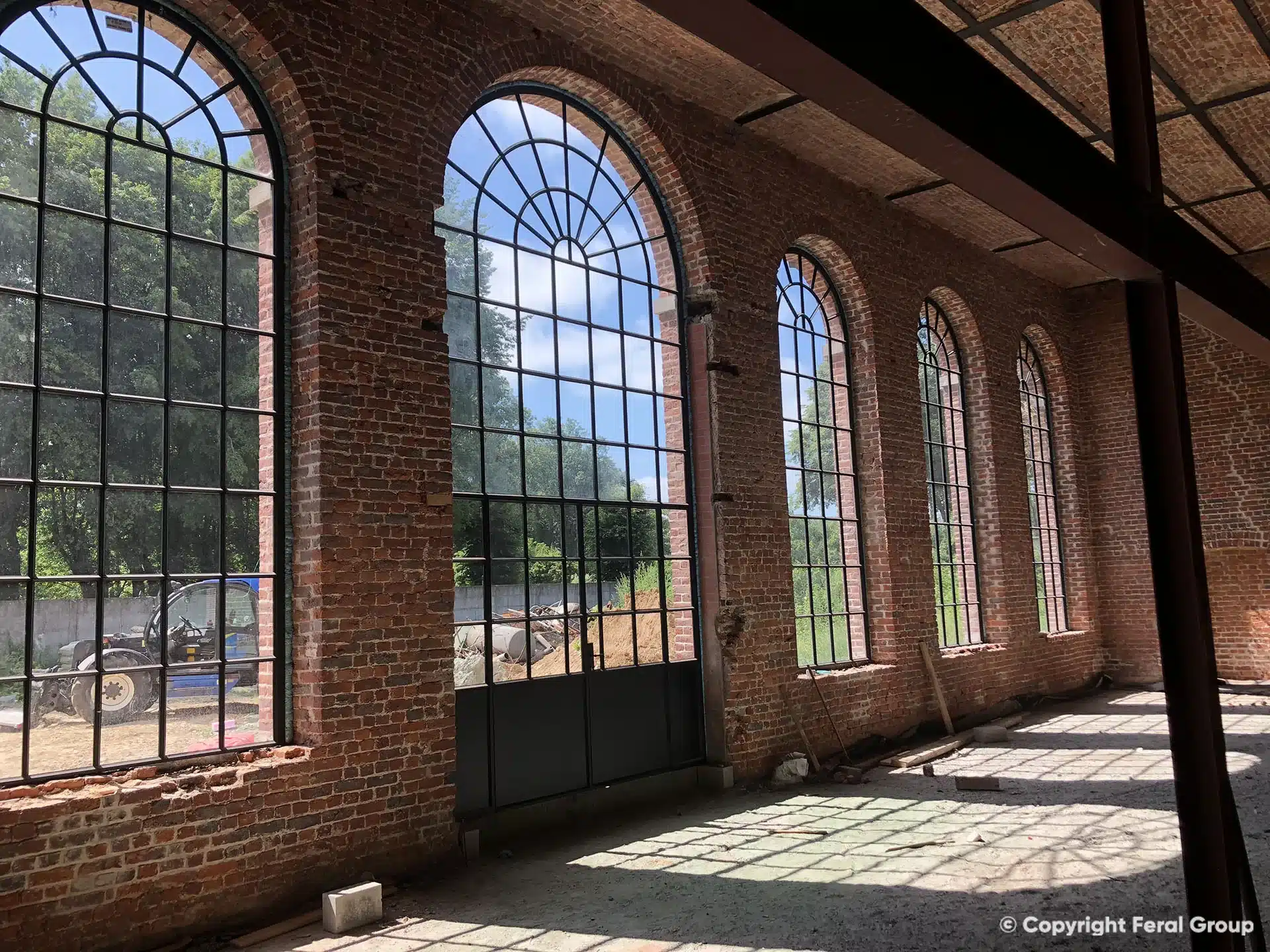 Orangerie van het kasteel van Moulbaix met XL smeedijzeren boogramen en een hoge deur, met zonlicht op de vloer.