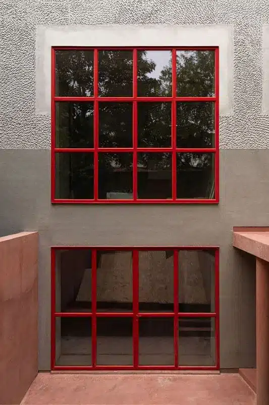 Frontaal zicht op een groot rood stalen raam boven een gesloten stalen deurpui, afgemastiekt in RAL 3000.