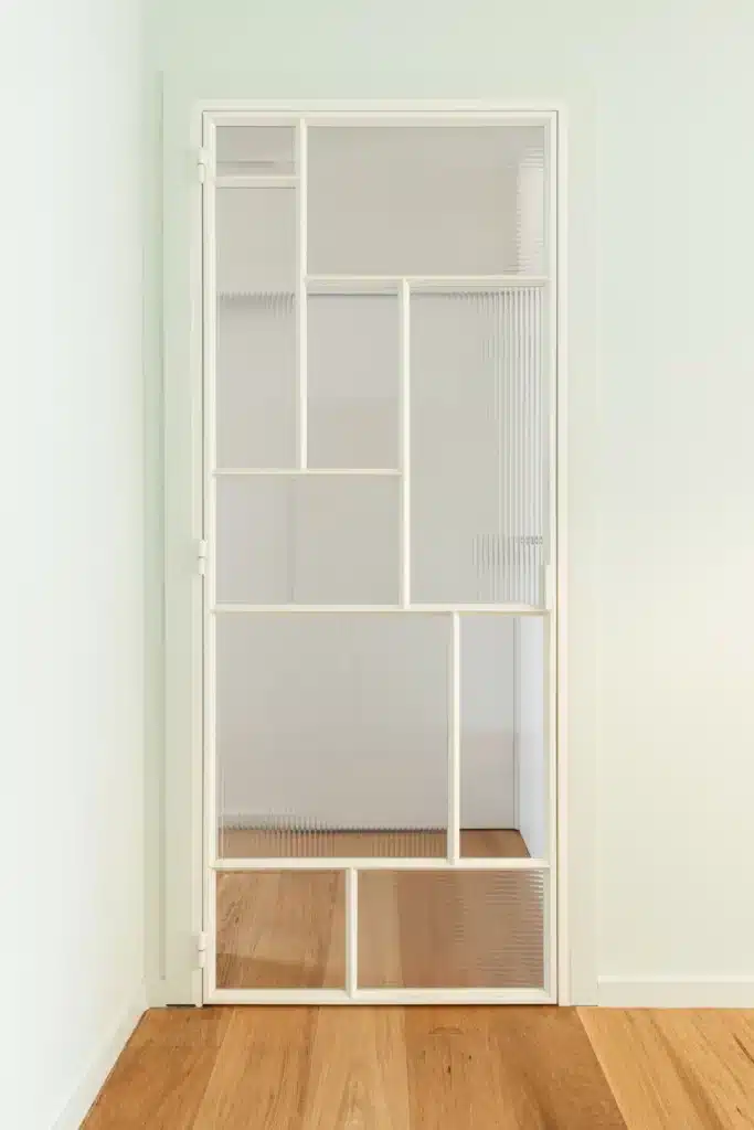 Gesloten stalen binnendeur in gebroken wit met asymmetrische vlakverdeling en cannelé glas, in een woning.