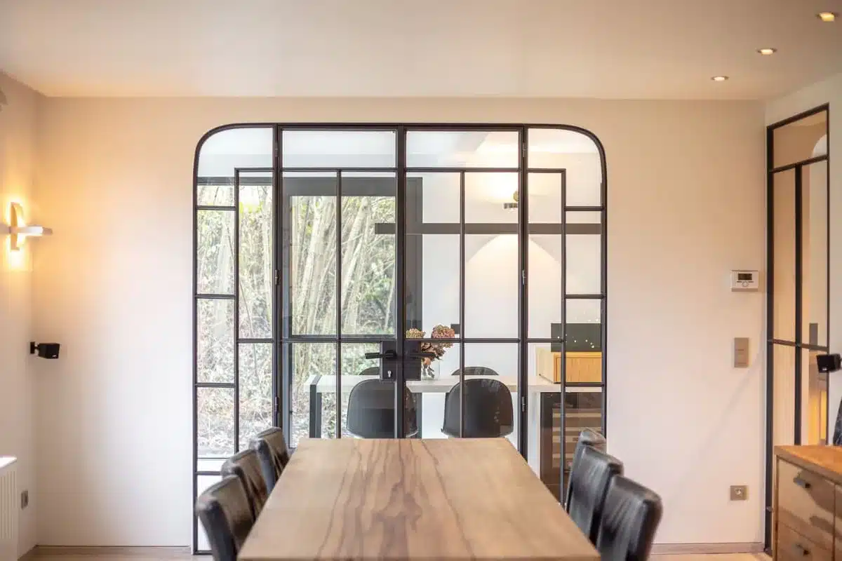 Stalen binnenpui met afgeronde hoeken en asymmetrische roedeverdeling achter de eettafel, in een renovatie.