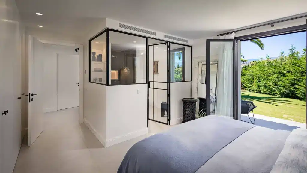 Slaapkamer met een stalen binnenraam naar de badkamer en een stalen deur die opent naar de tuin.