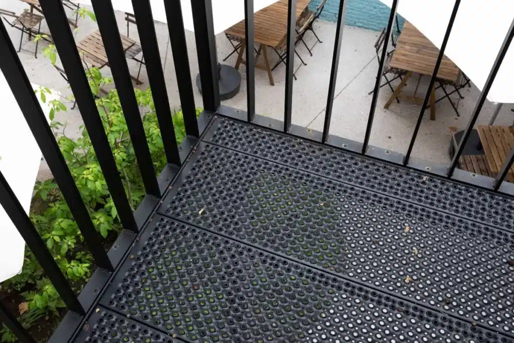Detail van het stalen bordes met geperforeerde vloerplaat en spijlen, met zicht op het terras beneden.