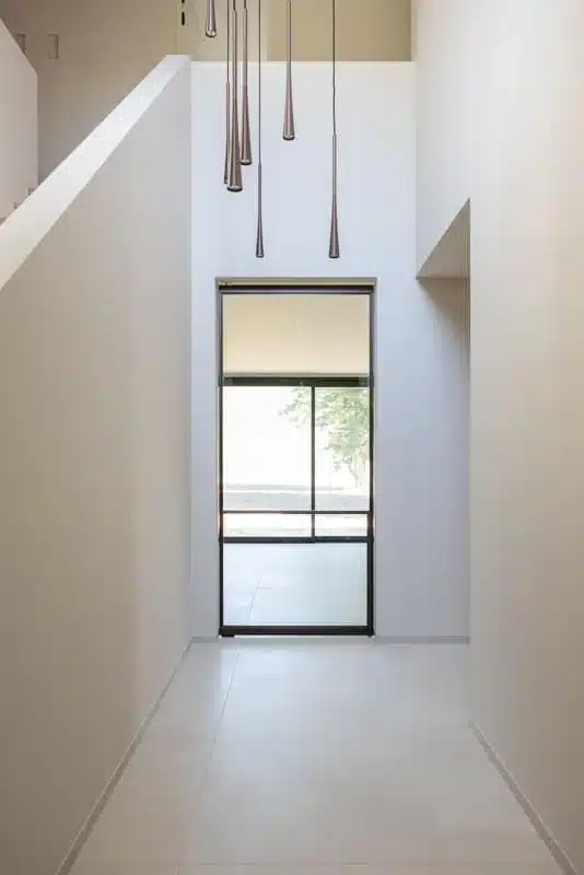 Hoge stalen deur met glas en tussenregel aan het einde van de lichte inkomhal met vide, in een villa.