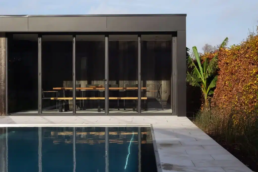 Stalen glasgevel met harmonicadeuren van het poolhouse, met het natuurstenen terras en het zwembad.