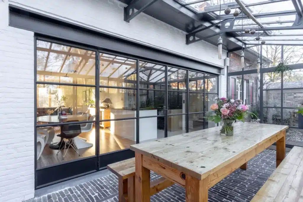 Stalen glaspui met roedeverdeling tussen de woning en de serre, met de eettafel in de serre ervoor.