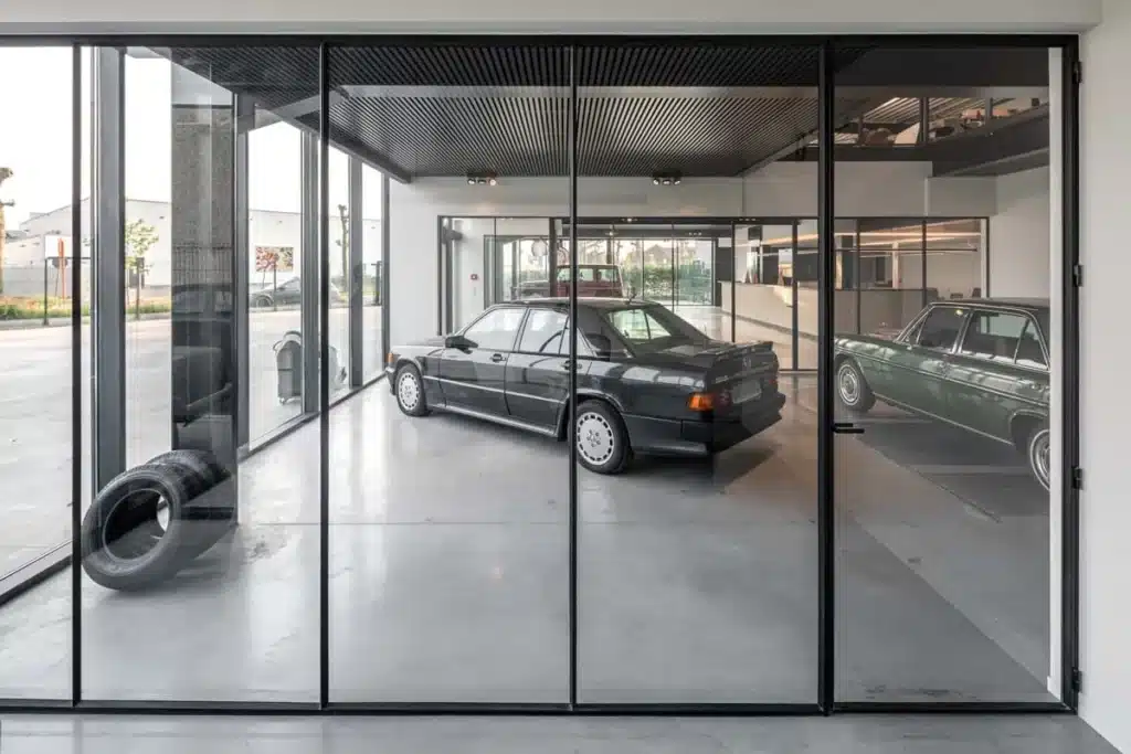 Stalen glaswand van vloer tot plafond met een oldtimer erachter, als transparante scheiding in de garage.