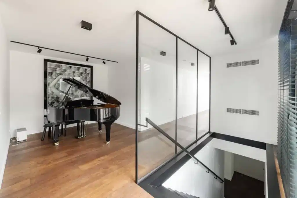 Stalen glaswand als borstwering rond het trapgat, met stalen leuning en de muziekruimte met vleugelpiano.