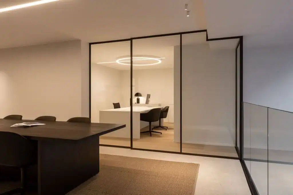 Schuin zicht op de stalen glaswand van het bureau achter de vergadertafel, naast de glazen balustrade.