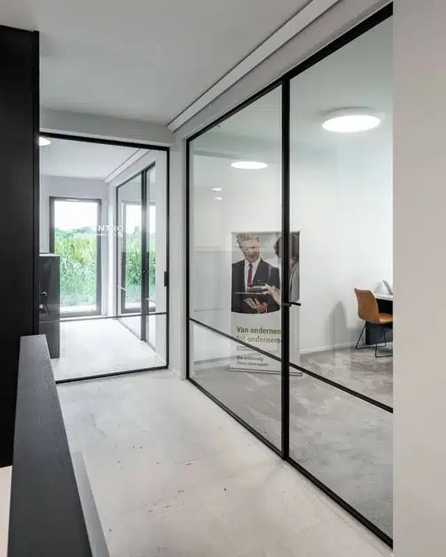Stalen glaswand met deur op de hoek van een kantoor, met superslanke profielen tot tegen het plafond.