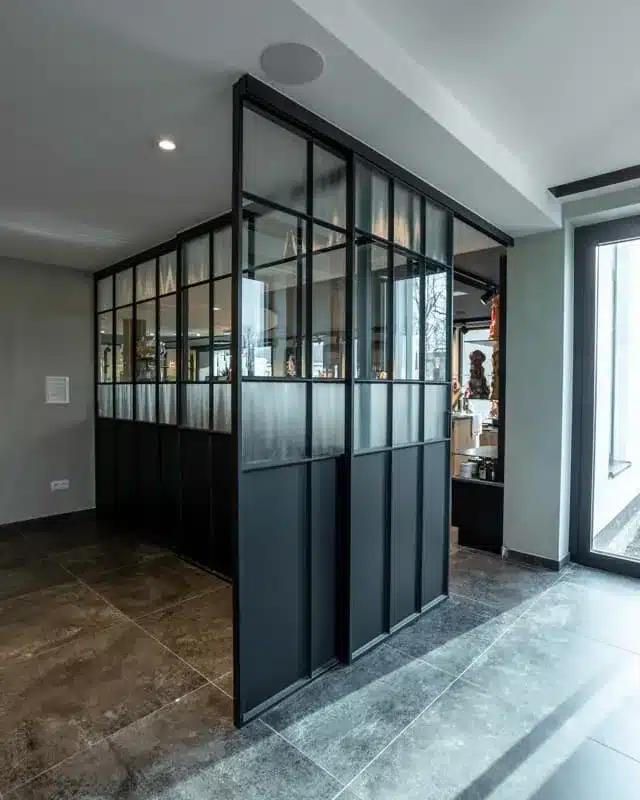 Hoekoplossing van een zwarte stalen glaswand die het atelier afschermt van de winkelruimte.