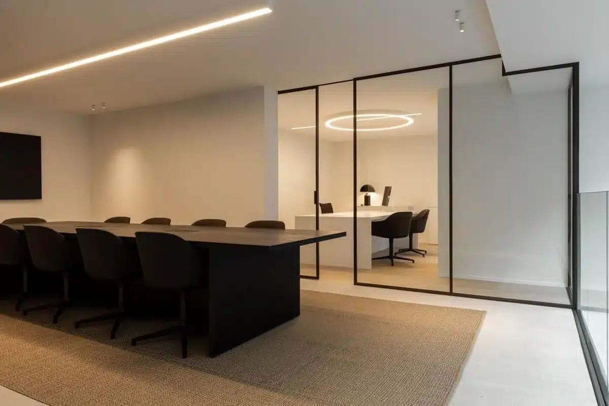 Vergaderzaal in een gerenoveerd kantoor, met achteraan een stalen glaswand rond een afgesloten bureau.