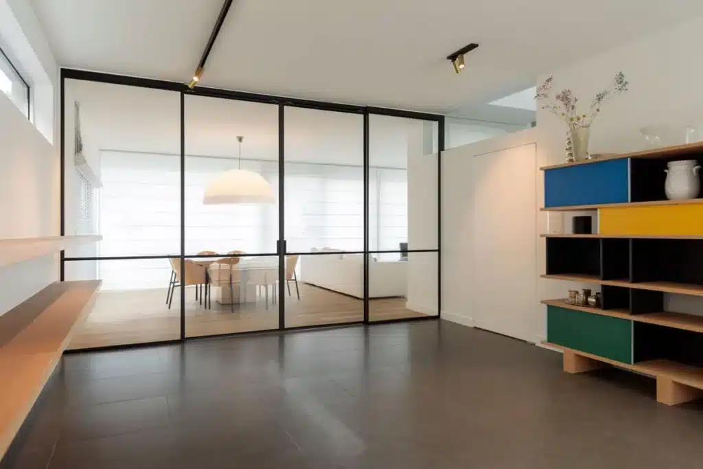 Overzicht van de ruimte met een stalen glaswand en schuifdeuren tussen hal en eetkamer, naast een kleurrijke kast.