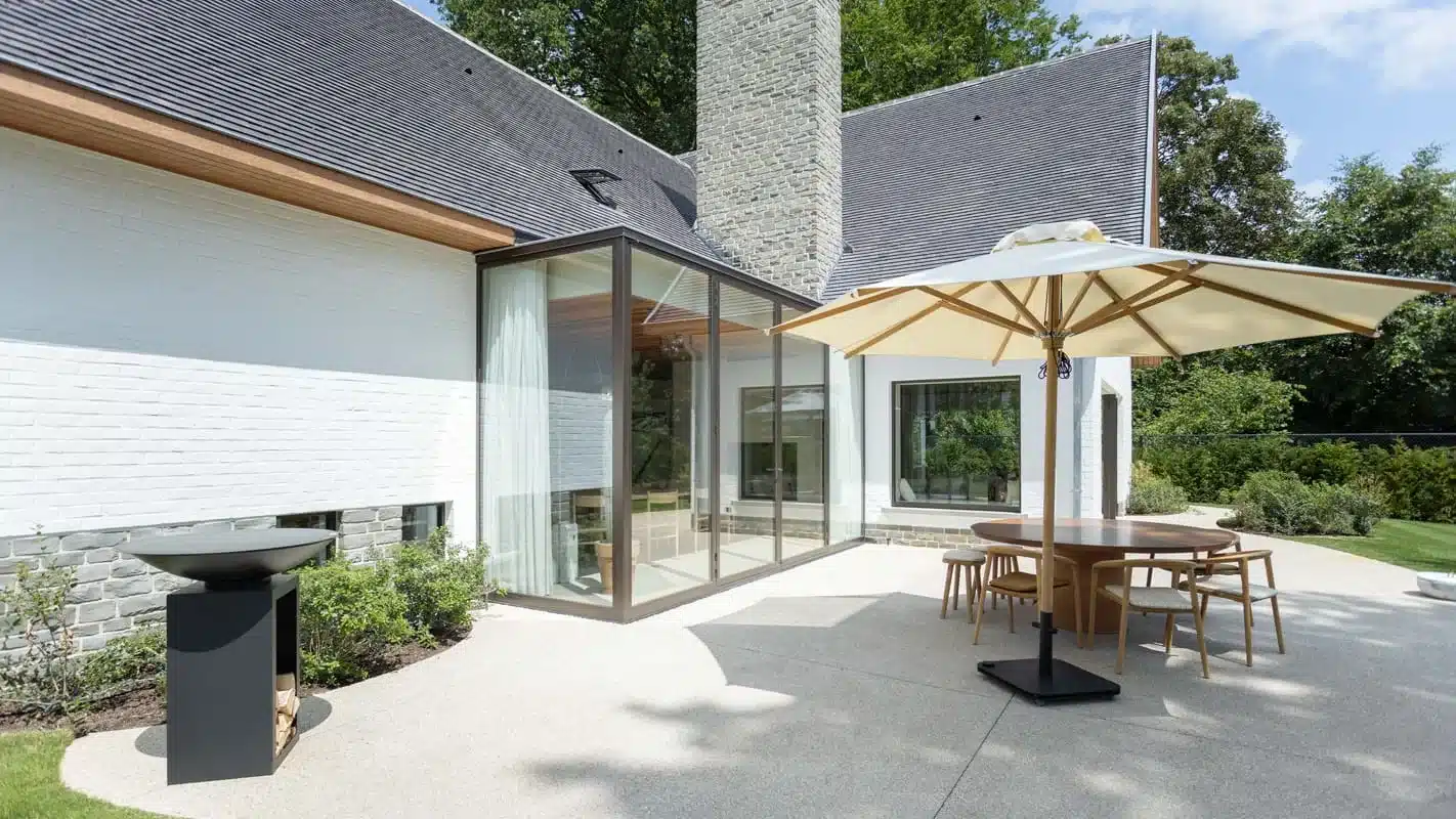 Uitbouw aan de tuinzijde met thermisch onderbroken stalen hoekpui, naast het terras met eettafel en parasol.