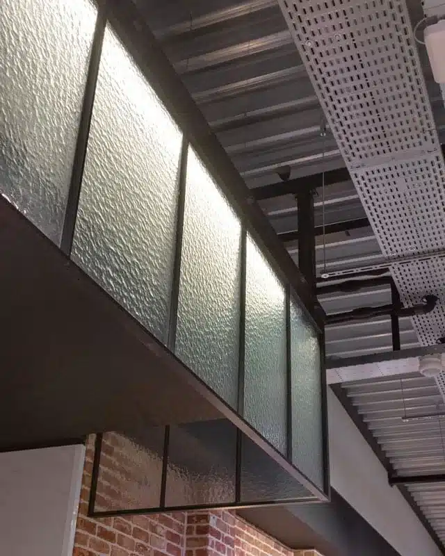 Staand detail van het stalen kader met kathedraalglas, van onderaf gezien langs de bakstenen wand.