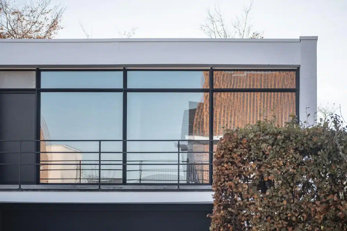 Brede stalen raampartij met slanke profielen achter een zwarte stalen balustrade op het terras.
