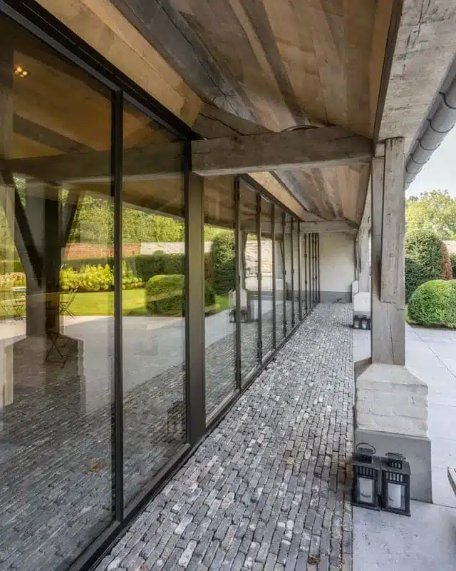 Stalen raampartij met eigen ontworpen onderdorpel boven de kasseivloer, met de tuin achter het glas.