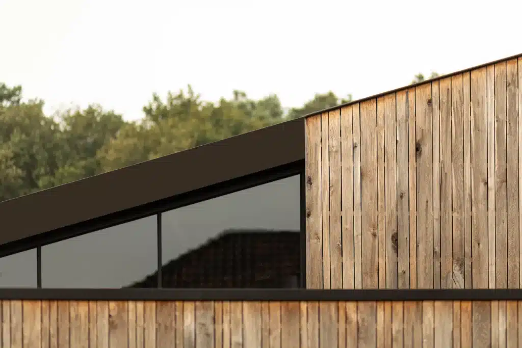 Horizontale stalen raamstrook onder de schuine dakrand, tussen de verticale houten gevelbekleding.