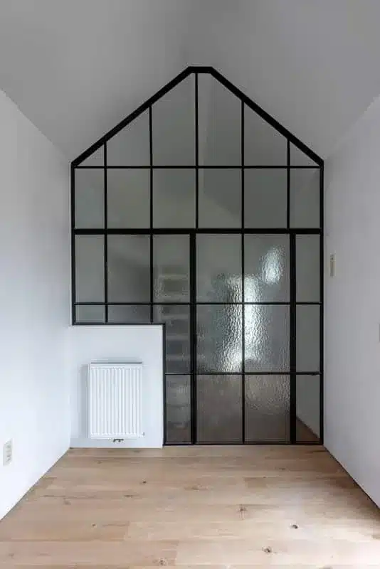 Stalen roomdivider in gelaagd kathedraalglas die tot in de nok van het zadeldak doorloopt.