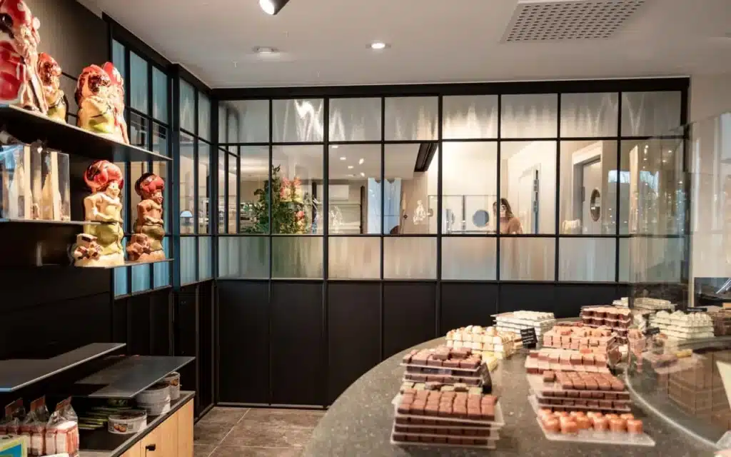 Zwarte stalen scheidingswand met helder glas en structuurglas tussen de chocolaterie en het atelier.