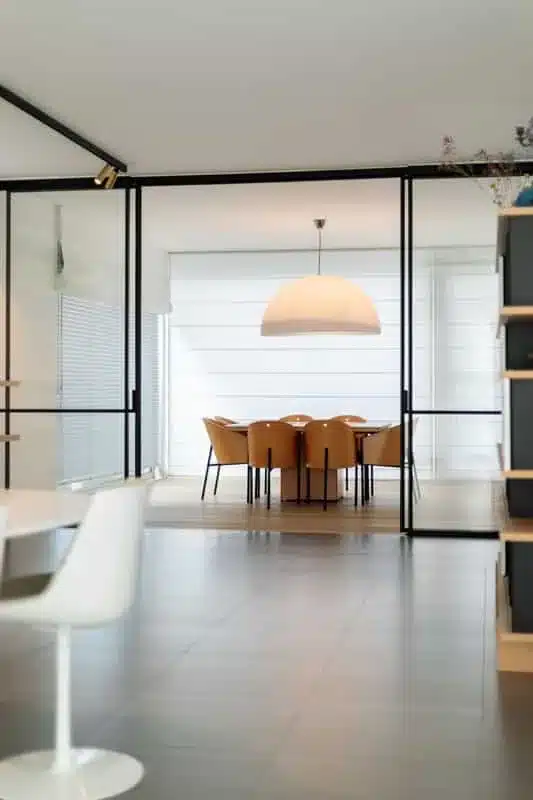 Staand zicht op de stalen room divider met schuifdeuren, met een witte stoel op de voorgrond en de eetkamer erachter.