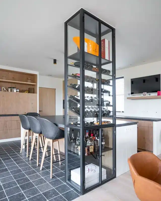 Hoge stalen wijnkast met glazen deuren naast het keukeneiland, met bovenaan een paar exclusieve flessen.