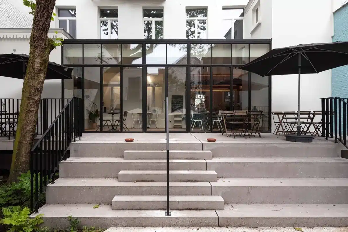 Verhoogd terras met brede trappen en zwarte stalen balustrades met leuning voor de stalen achtergevel.