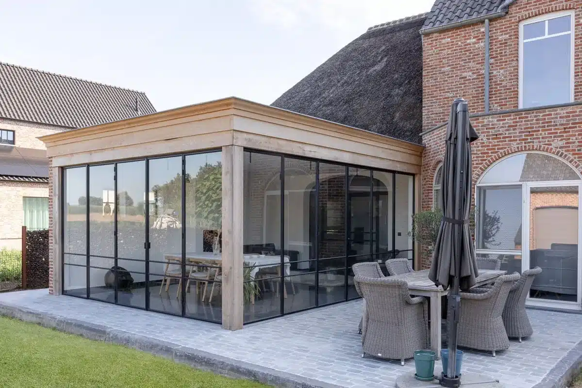 Tuinkamer met eiken kroonlijst tegen een woning met rieten dak, rondom afgesloten met stalen harmonicadeuren.