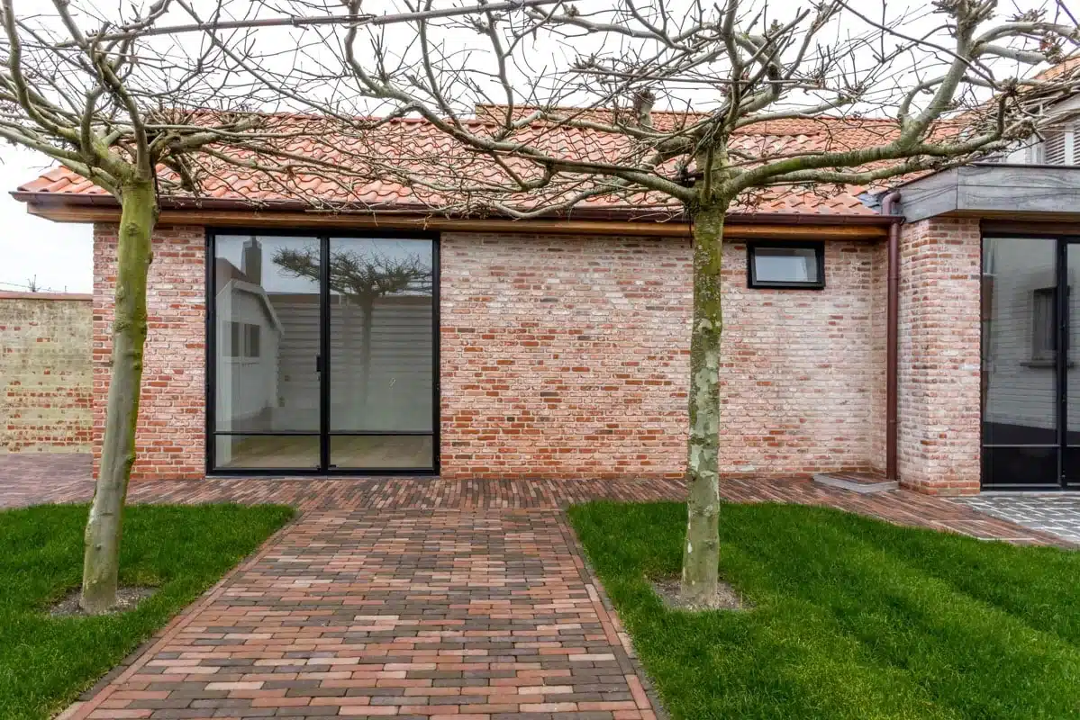 Villa in De Haan met rode baksteen en pannendak, met thermisch onderbroken stalen raamdeuren naar de tuin.