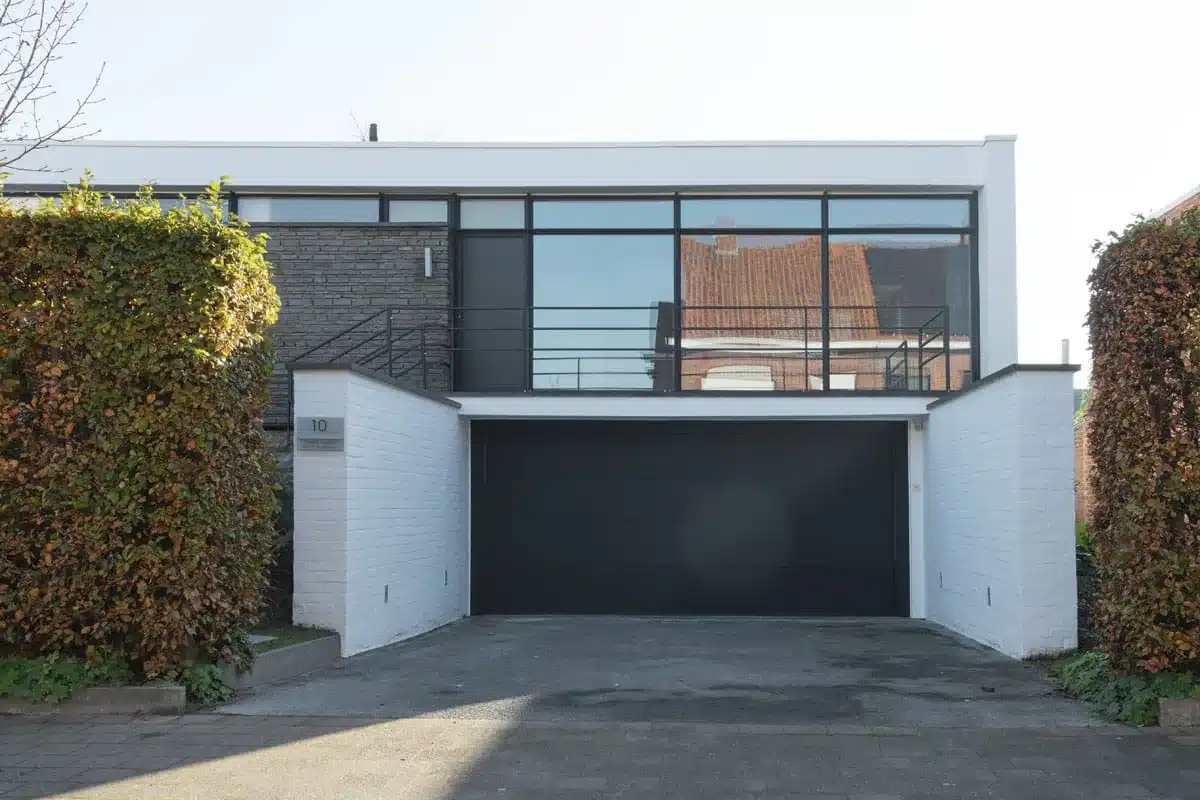 Voorgevel van een jaren 60-villa met een lange band stalen ramen boven de garage en tussen de hagen.