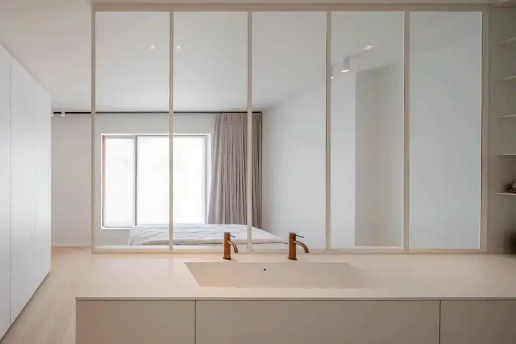 Witte stalen glaswand als afscheiding tussen slaapkamer en badkamer, met het lavabomeubel ervoor.